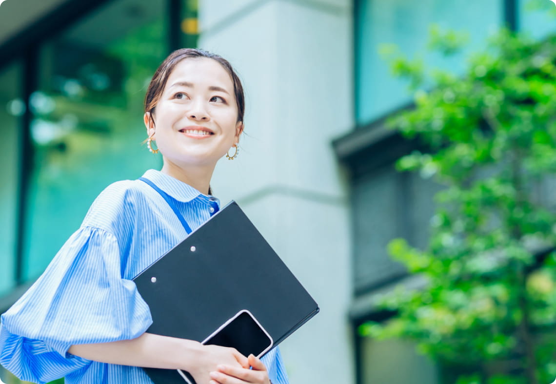 青空の下で書類を持つ笑顔の女性